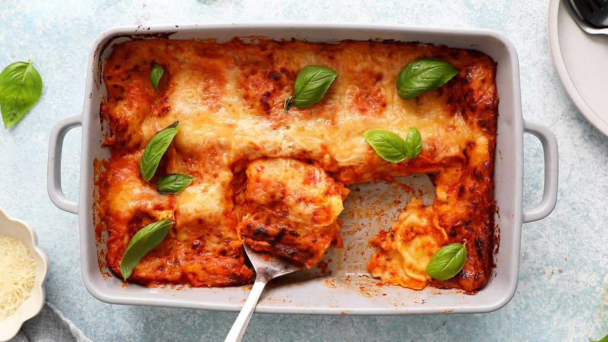 baked cheesy ravioli pasta garnished with green basil leaves in a grey baking dish.