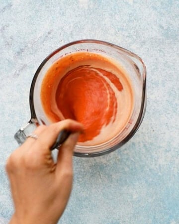 a hand mixing pink sauce in a glass bowl.