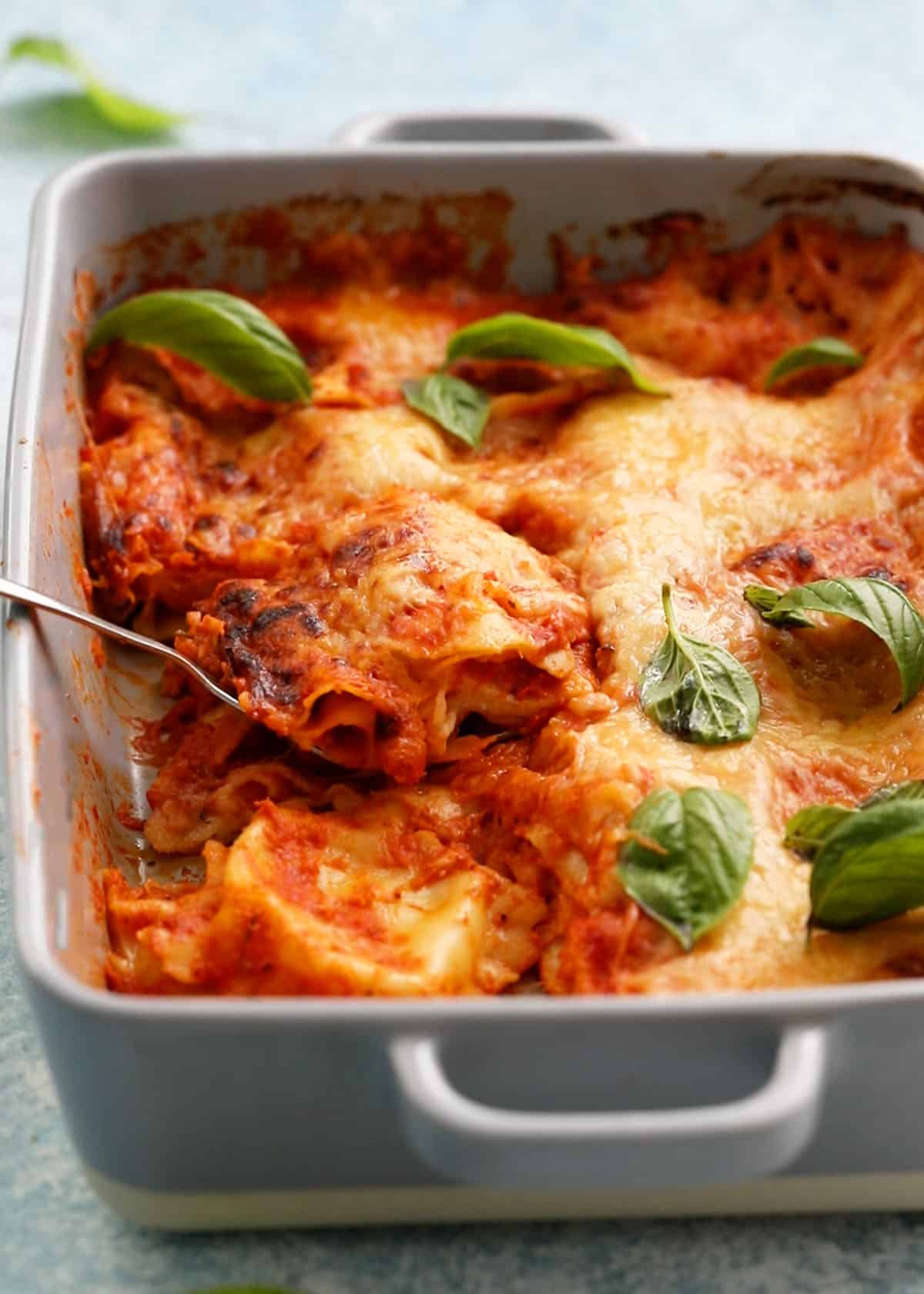 baked cheesy ravioli pasta garnished with green basil leaves in a grey baking dish.