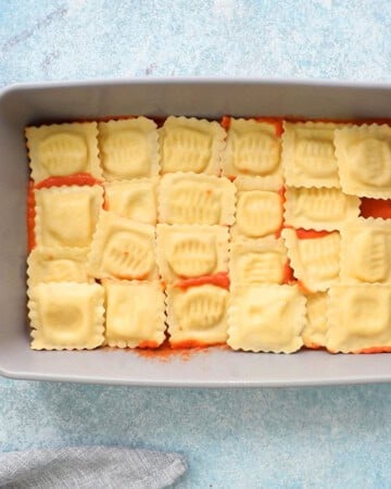 uncooked yellow ravioli pasta arranged in a grey baking dish.