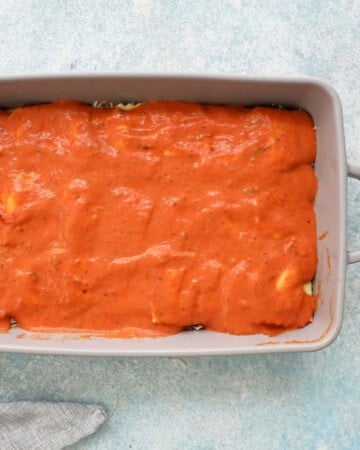 pink sauce spread on top of square ravioli pasta in a grey baking dish.