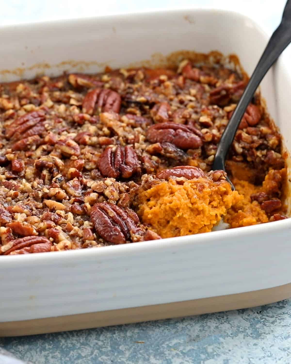 orange butternut squash casserole along with a black spoon in a white baking dish.