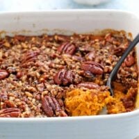 orange butternut squash casserole along with a black spoon in a white baking dish.