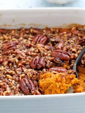 orange butternut squash casserole along with a black spoon in a white baking dish.