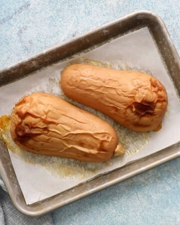 two roasted  butternut squash halves placed on a parchment lined baking sheet.