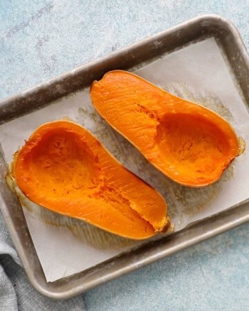 two roasted  butternut squash halves placed on a parchment lined baking sheet.