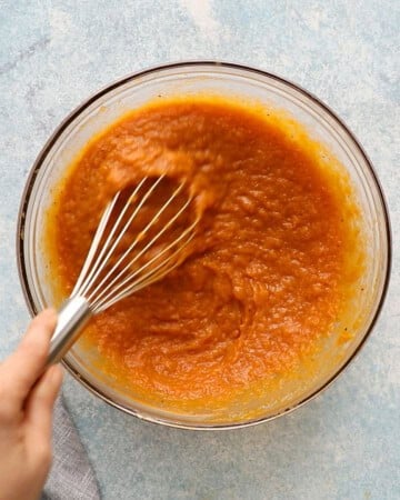 a hand whisking orange wet mixture in a glass bowl.