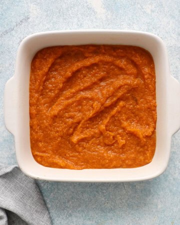 cooked orange butternut squash puree in a white ceramic square baking dish.