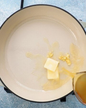 a hand pouring yellow stock into a large white pan. 