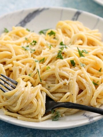 cooked white pasta noodles in a white plate along with a black fork.