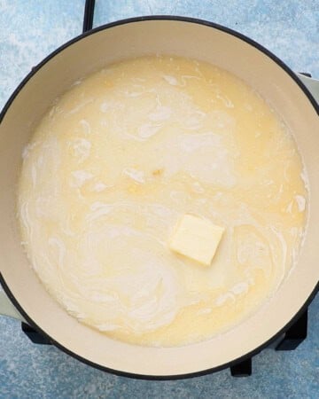 a square piece of butter and white liquid in a large white pan.