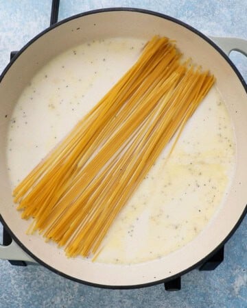 raw spaghetti noodles placed in some white liquid in a large white pan.