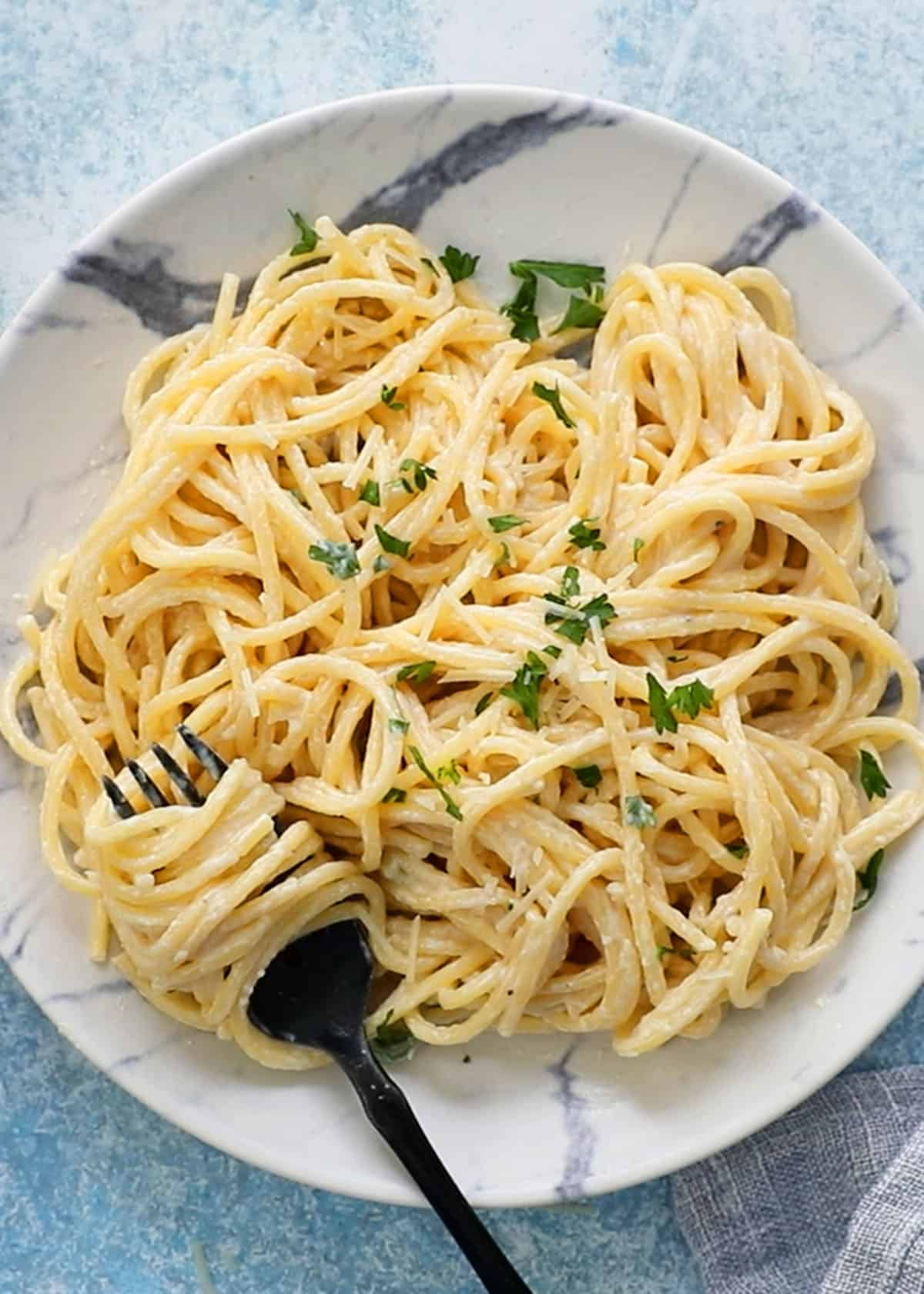 cooked white pasta noodles in a white plate along with a black fork. 