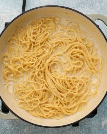 cooked spaghetti in white sauce in a large white pan.