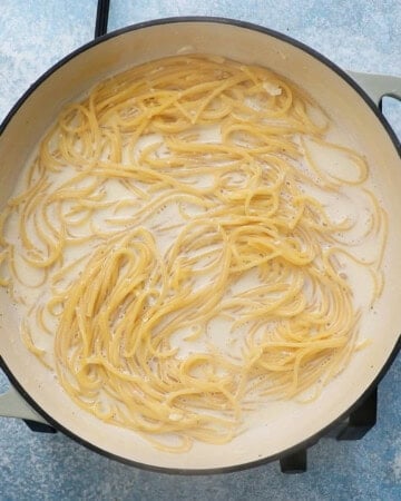 cooked spaghetti in white sauce in a large white pan.