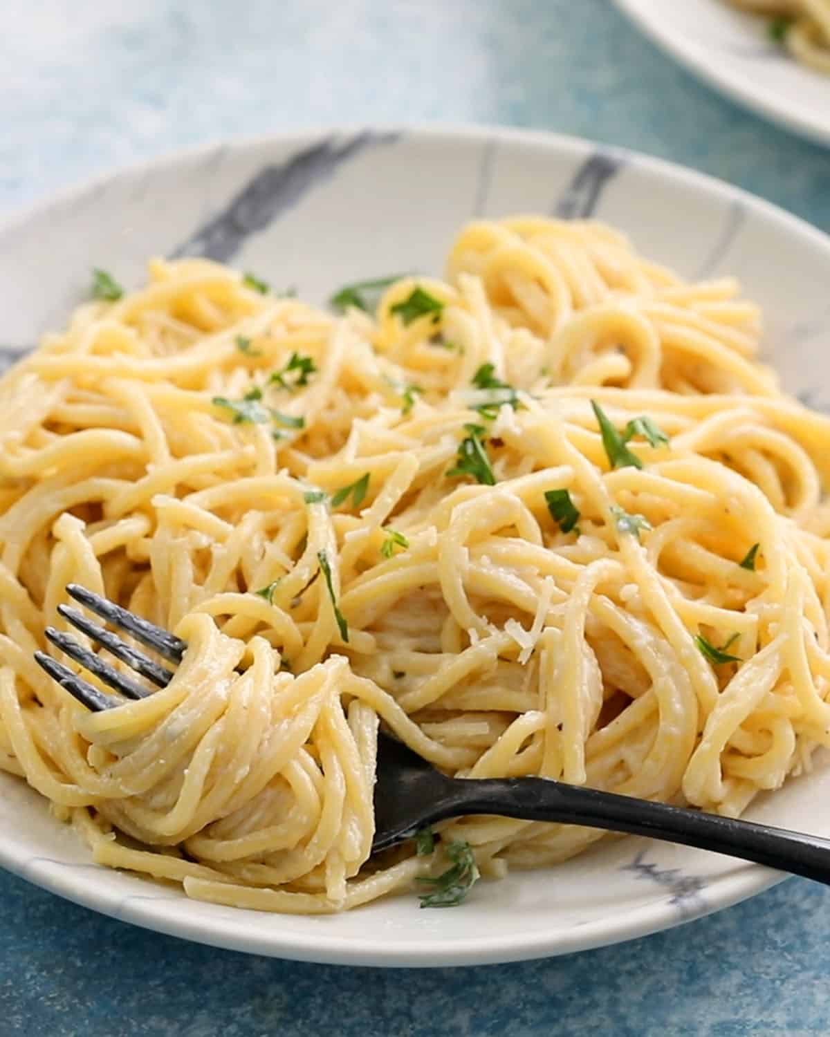 cooked white pasta noodles in a white plate along with a black fork. 