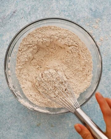 a hand whisking flour mixture in a glass bowl.