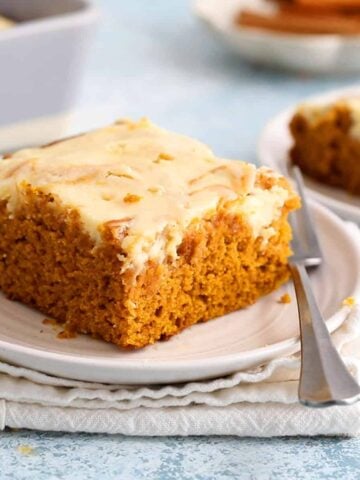 one slice of pumpkin cake topped with cream cheese in a white plate.