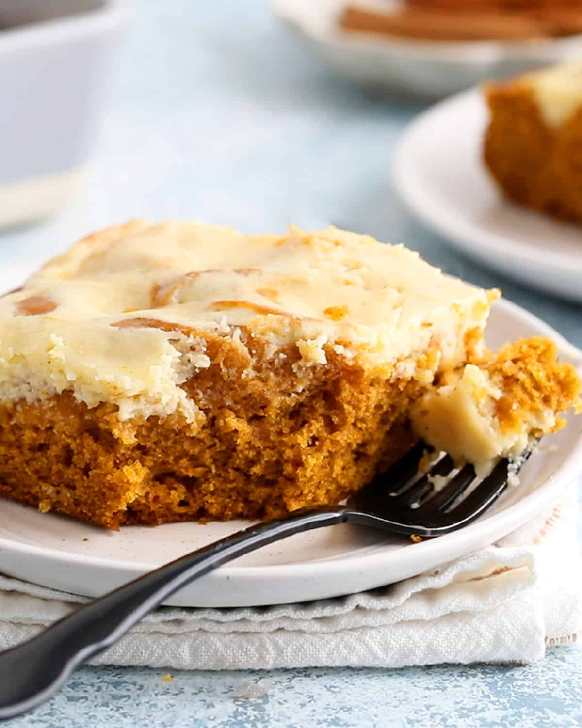 one square slice of pumpkin cake on a white plate along with a black fork.