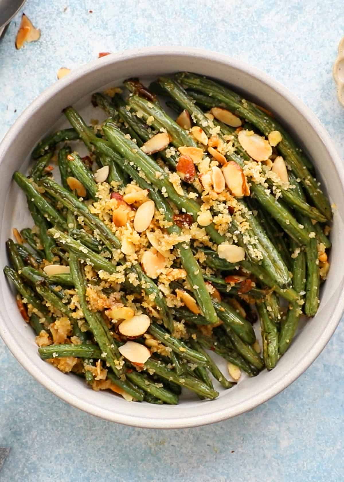 roasted green beans topped with almonds and panko in a white bowl.