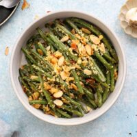 roasted green beans topped with almonds in a white bowl.