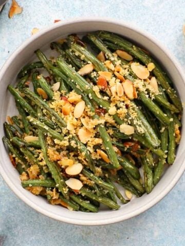 roasted green beans topped with almonds in a white bowl.