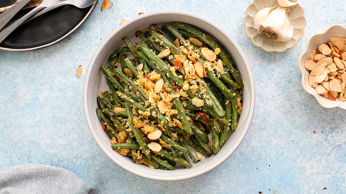 roasted green beans topped with almonds and panko in a white bowl.