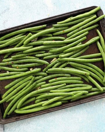 seasoned green beans in a black baking sheet.