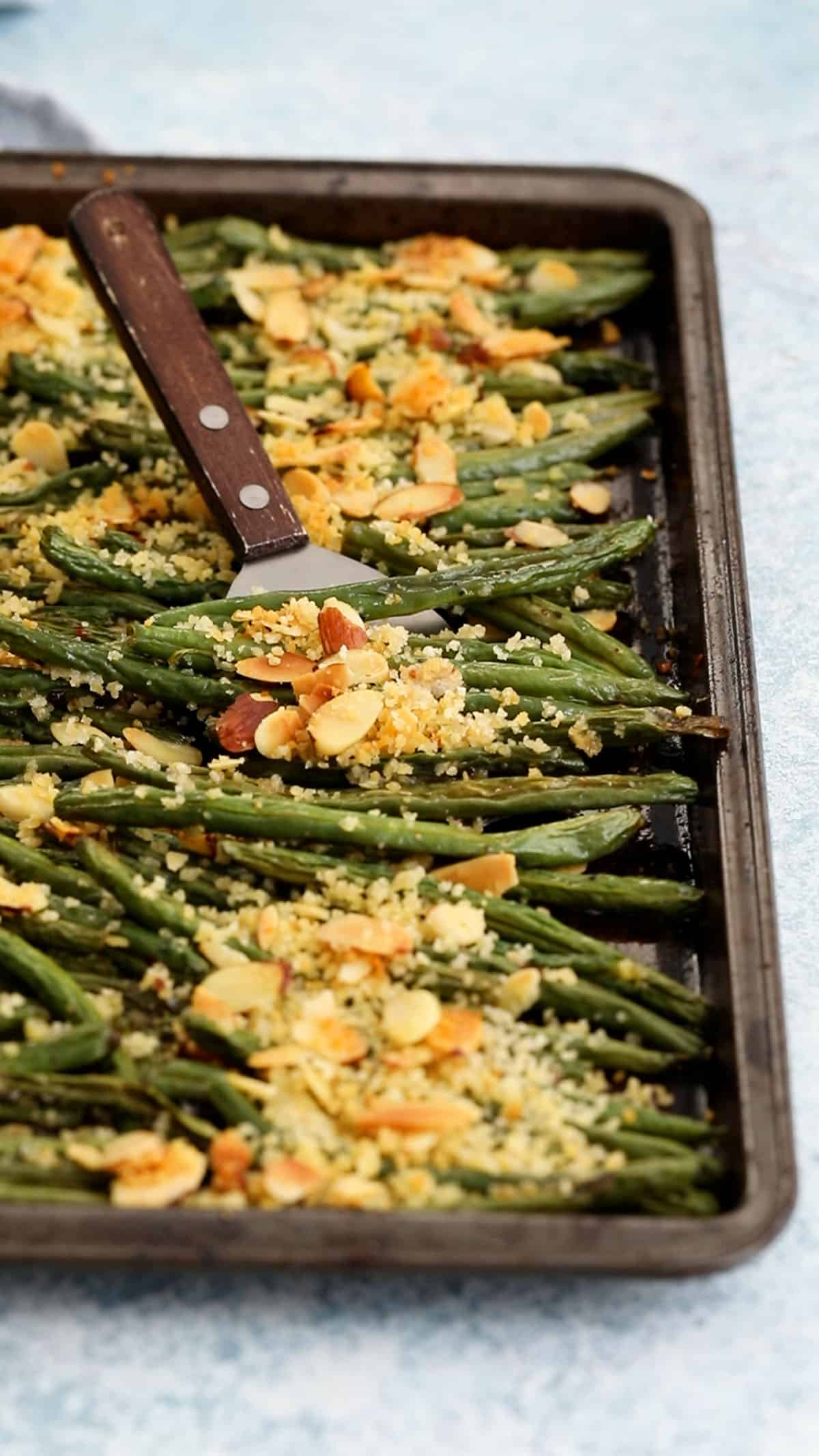 roasted green beans topped with panko in a black baking sheet.