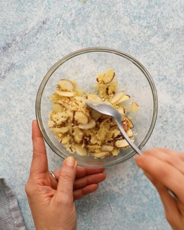 two hands mixing sliced almonds along with panko in a small white bowl.