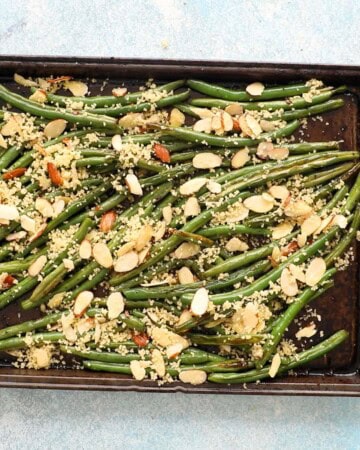 roasted green beans topped with sliced almonds in a black baking sheet.