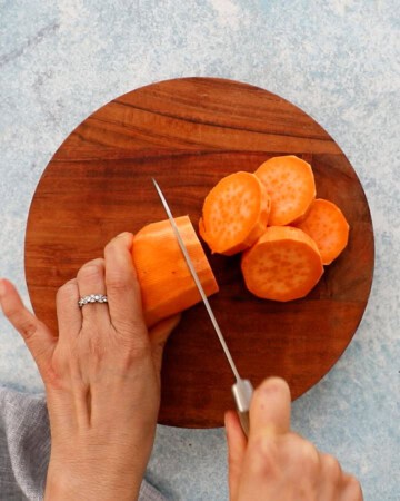 two hands slicing one sweet potato into rounds.