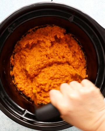 a hand mashing sweet potatoes in a black pot.